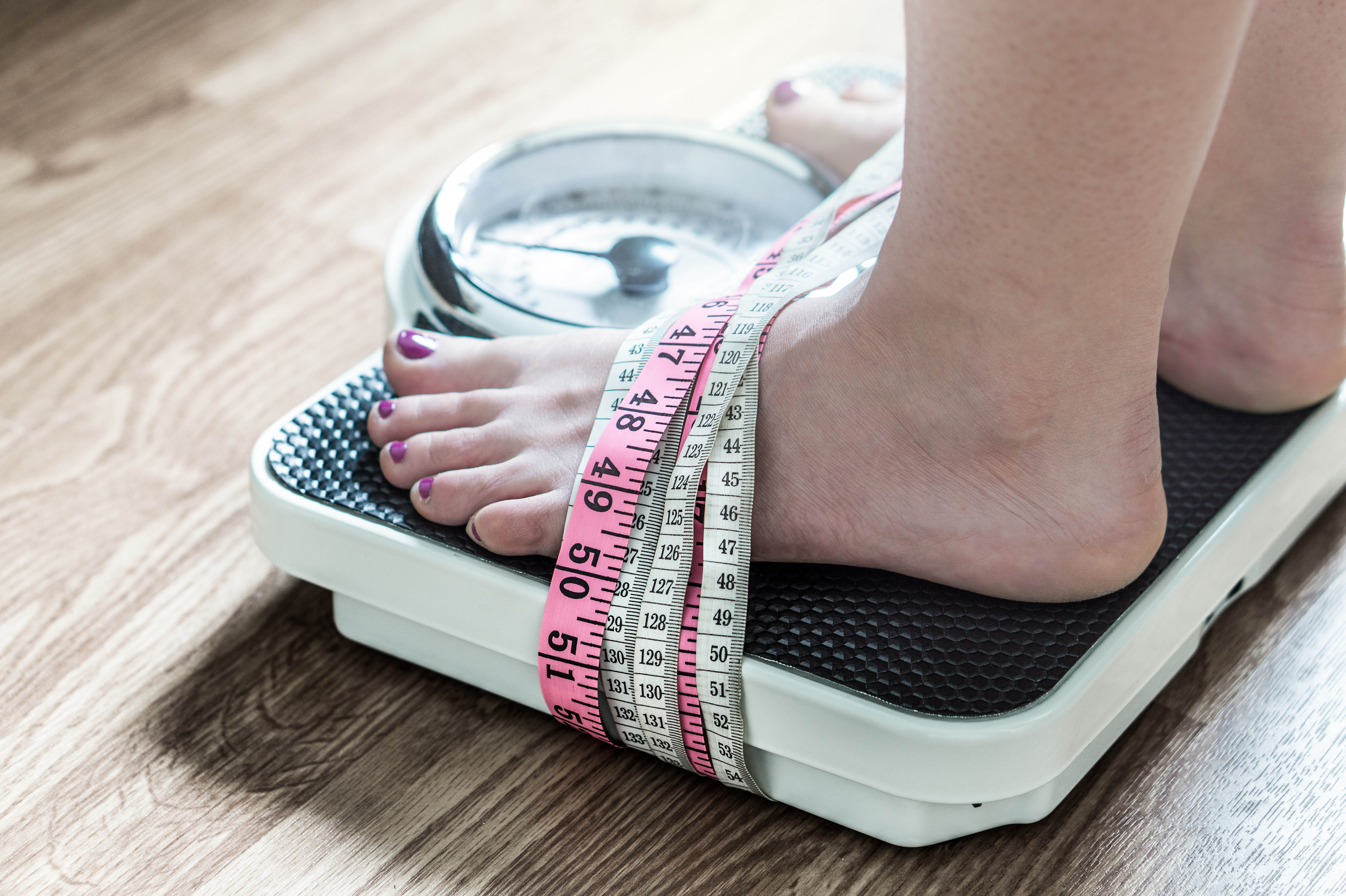 Close-up of woman's feet as she stands on a scale, with tape measures wrapped around her feet and the scale